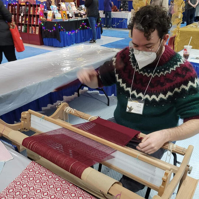 Christian working on their rigid heddle loom creating a red wool scarf